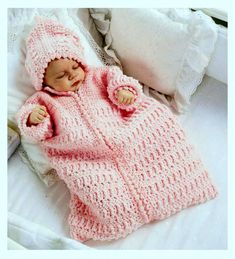 a baby in a pink knitted blanket laying on a bed