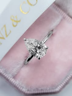 an engagement ring with a pear shaped diamond on it's side in a pink velvet case