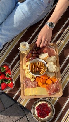 a person sitting at a table with cheese, crackers and strawberries on it