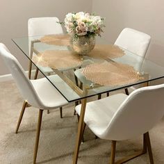 a glass dining table with white chairs and flowers on top in a room that has carpeted flooring