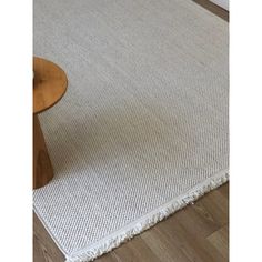 a white rug on the floor with a wooden table and chair in front of it