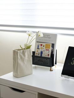 a white vase with flowers sitting on top of a desk next to a clock and calendar