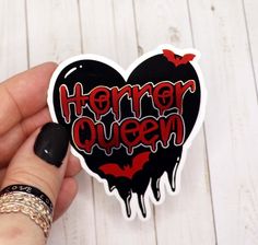 a hand holding a heart shaped sticker with the word horror queen painted on it