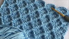 a crocheted blue blanket next to a ball of yarn and a knitting needle