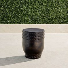 a large metal vase sitting on top of a cement floor next to a green hedge