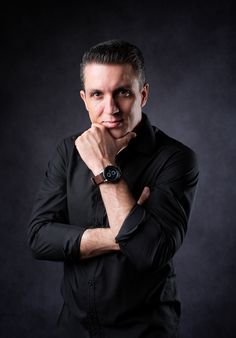 a man is posing with his hands on his chin and looking at the camera while wearing a black shirt