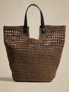 a brown woven bag with black handles on a beige background, it is made out of jute and leather