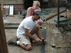 a man and woman are working on something in the dirt with a measuring tape next to them