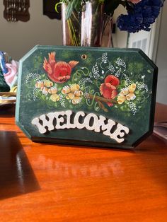 a welcome sign sitting on top of a wooden table next to a vase with flowers