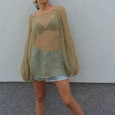 a woman standing in front of a white wall wearing a green sweater and denim shorts