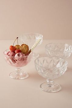 three glass bowls filled with ice cream and cherries on top of a white table