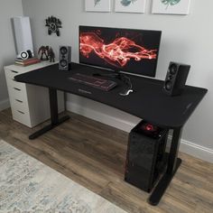 a computer desk with speakers and a monitor on it in front of a wall mounted art piece