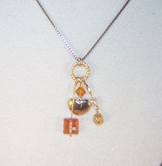 "A silver 17\" gold necklace with a pendant of various charms, crystals and gemstones. This pendant features a beautiful topaz Swarovski crystal bicone, a shining copper Stairway Swarovski crystal, a gold filigree bead, a small pearl heart, and a small gold heart all on a gold filled ring. Necklace has a gold chain with lobster claw clasp. Can be shortened or an extension can be added - please send message to seller when ordering if a length change is required." Gift Lariat Charm Necklaces, Lariat Charm Jewelry As Gift, Lariat Charms Jewelry Gift, Gold Crystal Lariat Necklace, Gold Crystal Heart Pendant Jewelry, Lariat Jewelry Charms As A Gift, Gold Metal Pendant Crystal Necklaces, Unique Gold Pendant Charm Necklace, Anniversary Pendant Jewelry With Dangling Charms