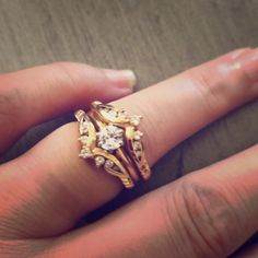 a woman's hand holding a gold ring with two diamonds on it and an engagement band