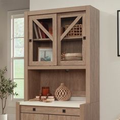 a wooden cabinet with glass doors and drawers in a room next to a potted plant