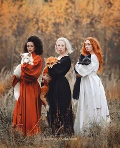 three women in long dresses are holding cats