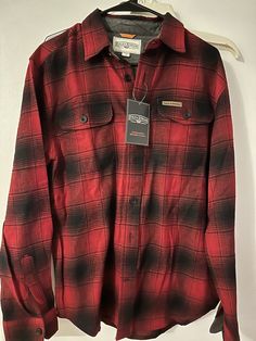 a red and black flannel shirt hanging on a hanger with a tag