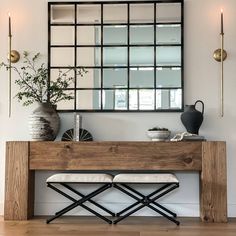 a wooden bench sitting under a mirror next to a vase on top of a table