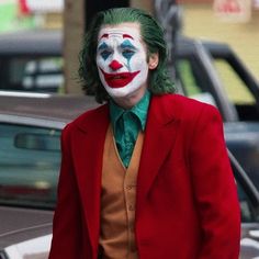 a man in a red suit and clown makeup is walking down the street with his hands in his pockets