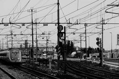 black and white photograph of trains on tracks in an industrial area with lots of wires