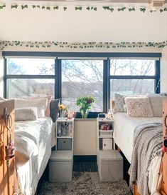 two beds in a room with large windows and plants on the nightstands, next to each other