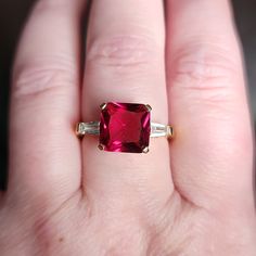 a close up of a person's hand holding a ring with a pink stone