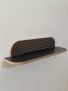 a wooden shelf mounted to the side of a white wall with black strips on it