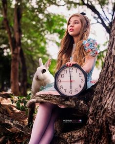 a woman sitting on top of a tree holding a clock