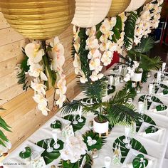 a table topped with lots of white flowers and greenery next to hanging lanterns on wooden walls