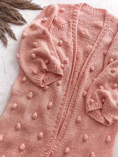 a pink cardigan with polka dots on it and a feather laying next to it