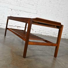 a wooden bed frame sitting in front of a white brick wall on concrete flooring