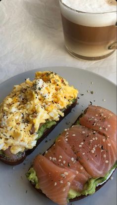 two pieces of bread with salmon and eggs on them next to a cup of coffee