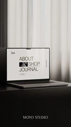 an open laptop computer sitting on top of a desk next to a window with the words about shop journal