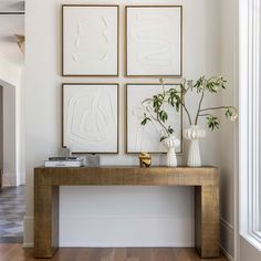 three white vases are sitting on a wooden table in front of four framed art pieces