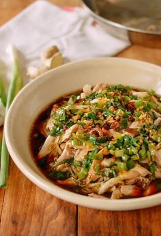 a white bowl filled with food sitting on top of a wooden table next to green beans