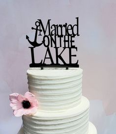 a white cake topped with a black sign that says married on the lake next to a pink flower