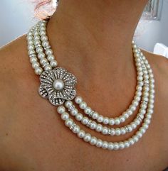 a woman wearing three strands of pearls with a flower brooch on it's neck