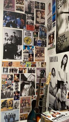 a guitar sitting on top of a wooden table next to a wall covered in posters