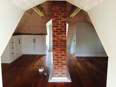 an empty room with wood floors and exposed brick chimney in the center, surrounded by white cabinets