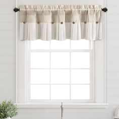 a kitchen window with white curtains and black hardware on the valance over the sink