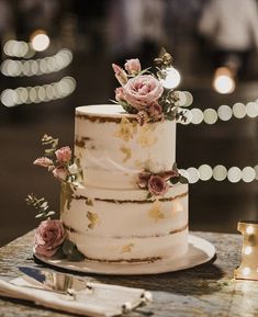 a three tiered cake with flowers on top is sitting on a table next to candles