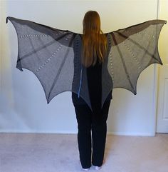 a woman standing in front of a door with a bat shaped shawl on her back