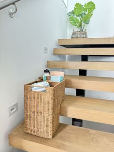 a basket sitting on top of a wooden stair case next to a potted plant