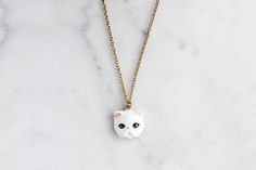 a necklace with a cat face on it sitting on a marble counter top next to a gold chain