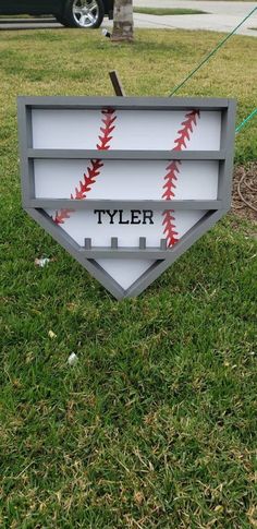 a baseball sign with the name tyler on it in front of a tree and grass