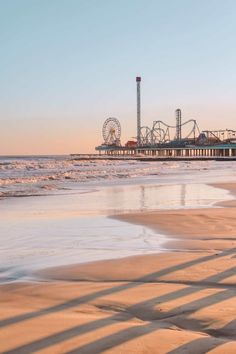 the sun is setting at an amusement park by the water's edge with roller coasters in the background