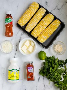 ingredients for corn on the cob laid out on a marble counter top with limes, butter, mayonnaise and seasoning