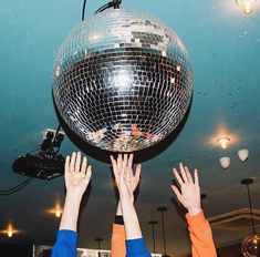 two people reaching for a disco ball in the air with their hands up to it