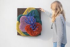 a woman standing next to a painting on the side of a wall with blue and red flowers