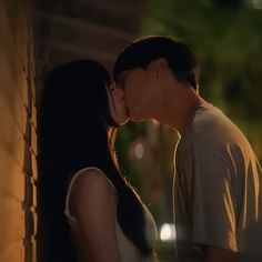 a man and woman kissing in front of a brick wall